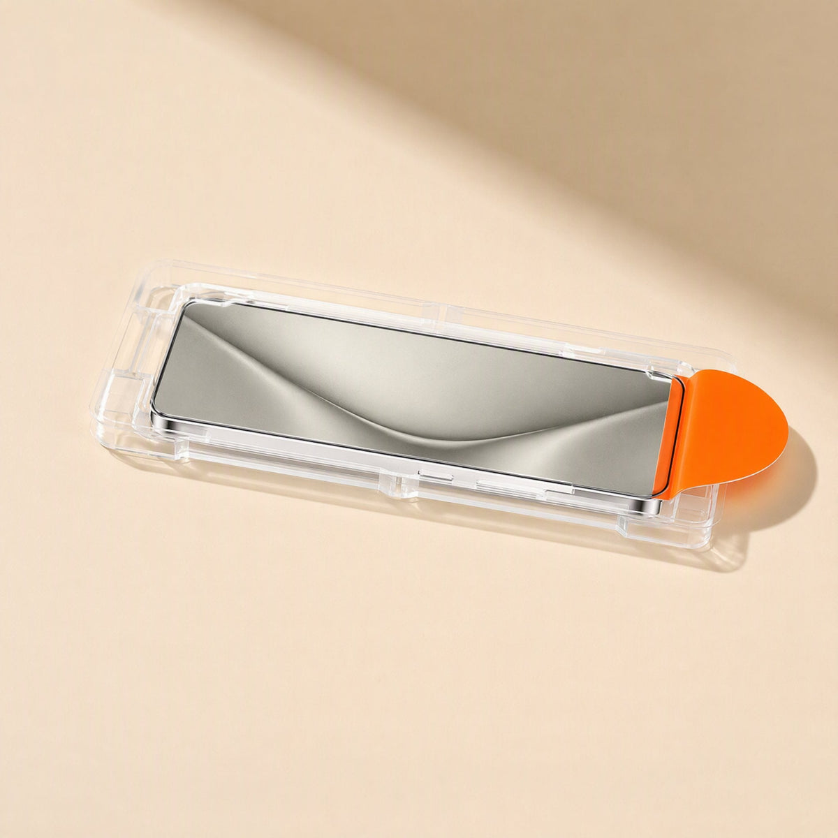 Clearshield – Side view of the glass protector seated in its clear installation tray with orange pull tab on a cream surface