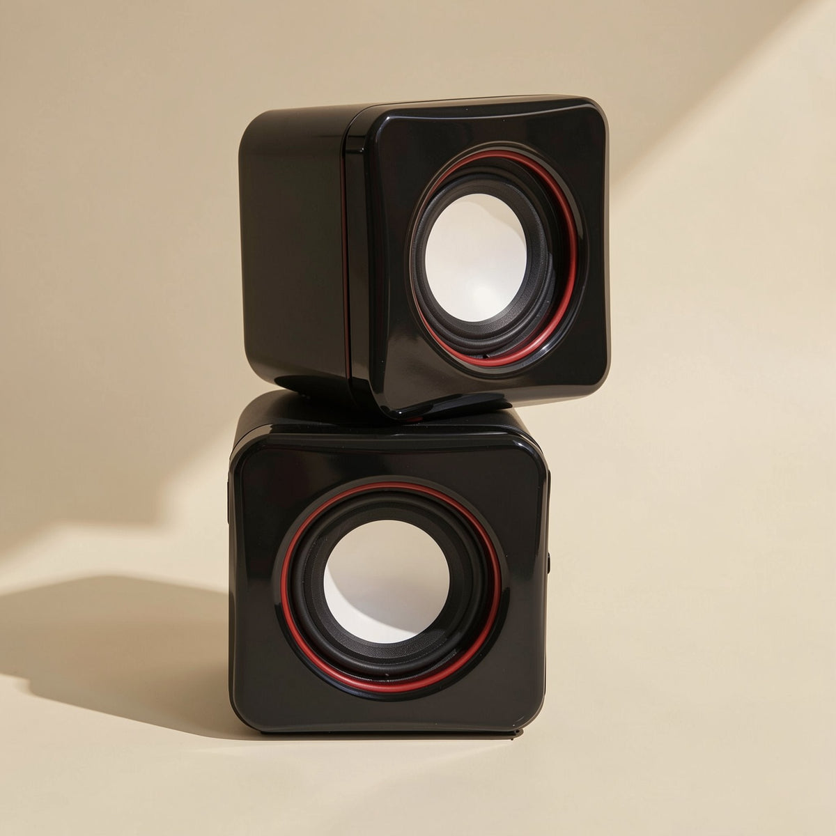 Desktune – Two black cube speakers stacked vertically, front cones facing out, with red rings on a plain cream backdrop