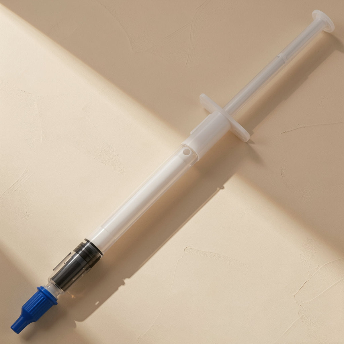 Heatpaste – Syringe with dark paste visible near the tip, blue screw cap attached, lying on a textured beige surface