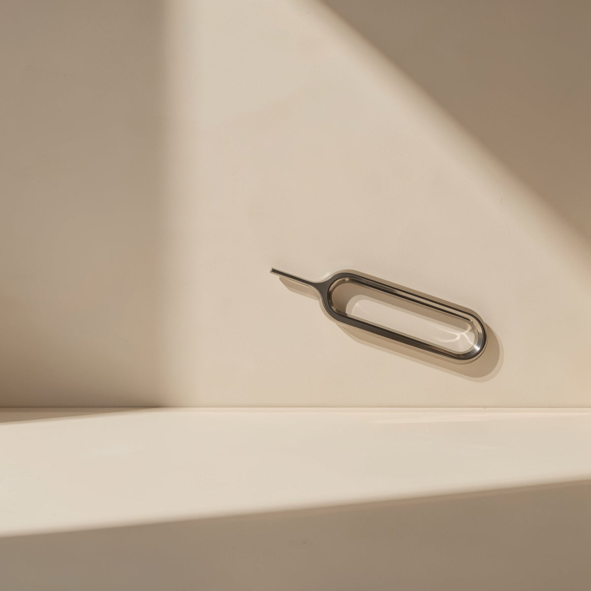 Screwbit – Slim metal SIM card ejector pin with an oval loop lying on a cream surface in soft shadow