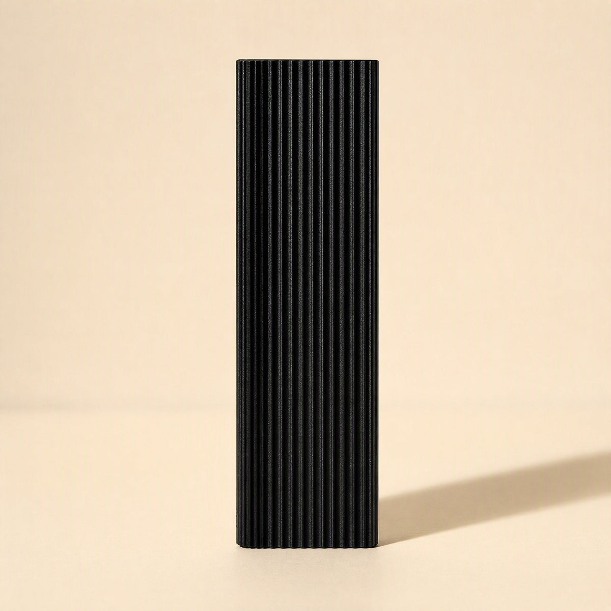 Ministore – Black ribbed external drive standing upright against a cream backdrop, casting a long shadow