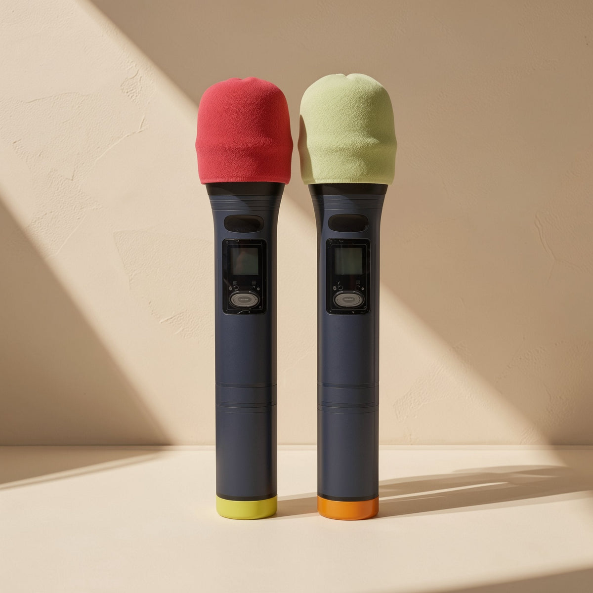 Curvehush – Red and light green sponge covers fitted on two dark handheld wireless microphones