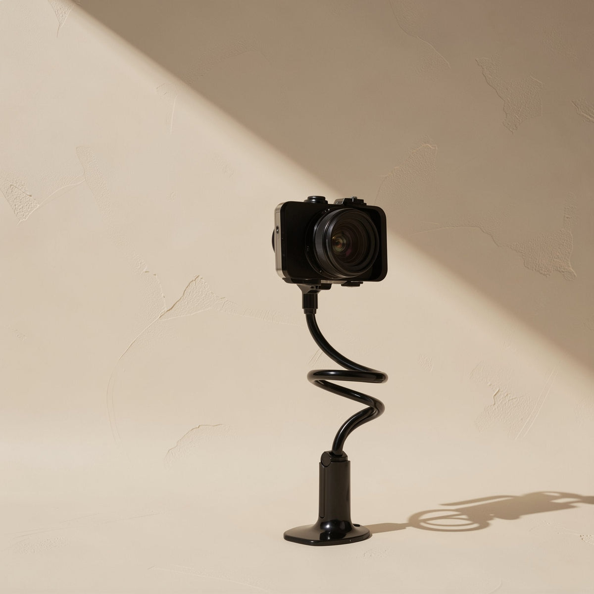 Tiltprop – Black coiled spiral arm on a round base holding a compact camera against a beige wall