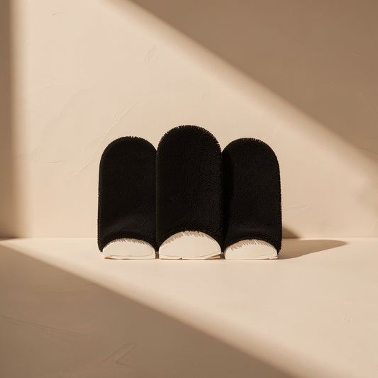 Tapfiber – Three black fuzzy finger sleeves standing upright against a cream wall with sunlight shadows