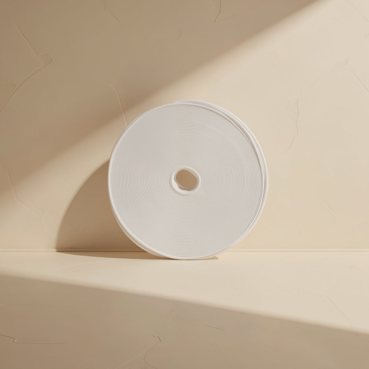 Wrapcord – White roll of hook-and-loop tape standing on edge against a cream wall, seen from the front