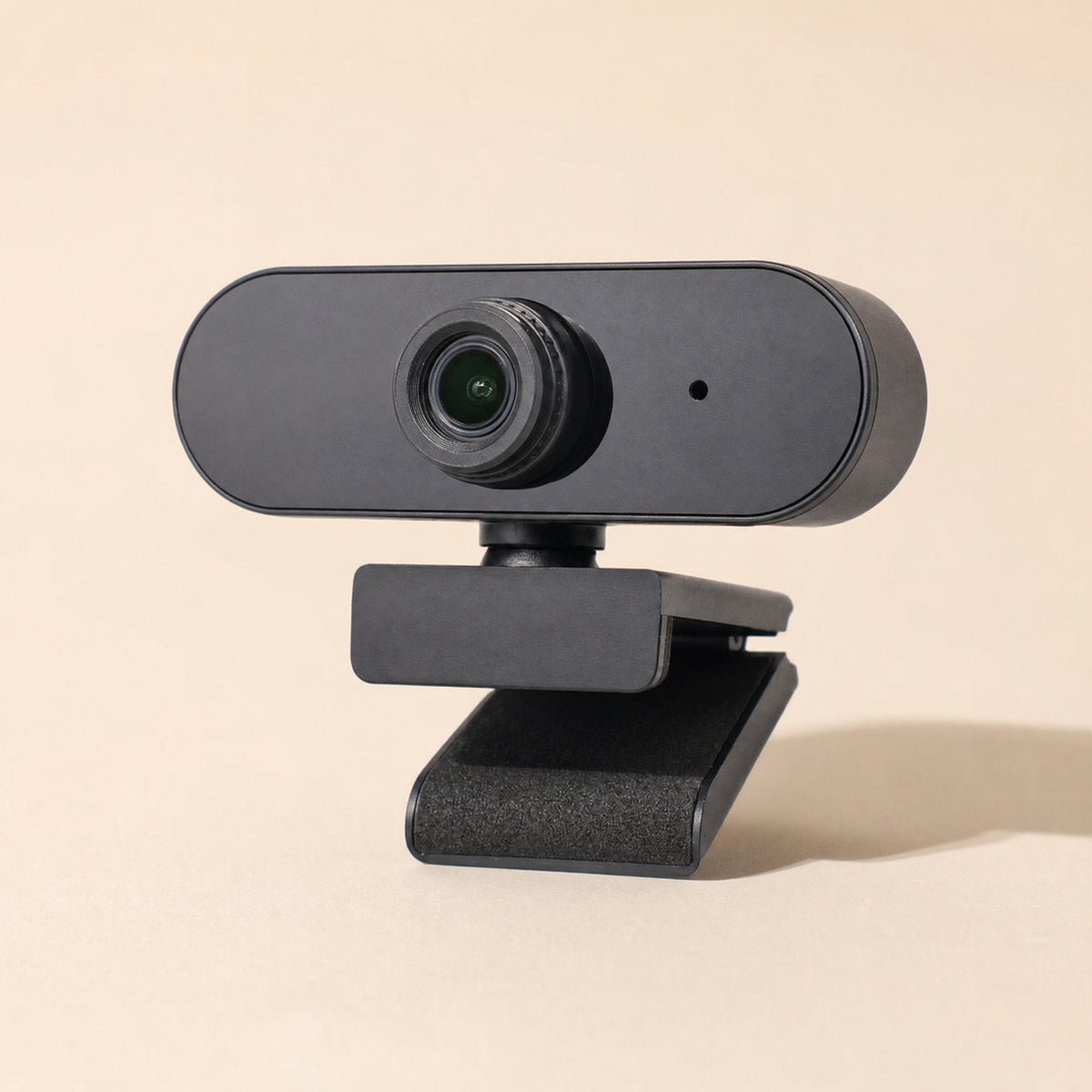 Talkview – Front view of the black clip-on webcam with round lens, microphone dot and foam-padded base on a peach backdrop