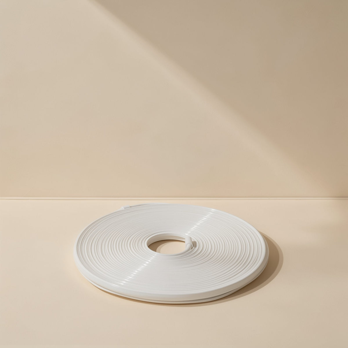Neonflex – Unlit white neon light strip wound into a flat disc, shown with its end tucked in on a cream background