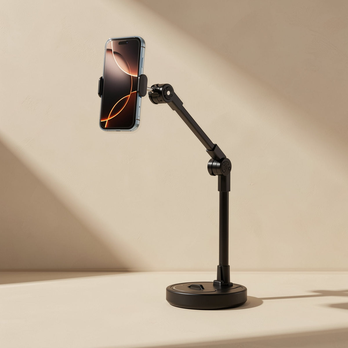 Hoverhold – Black stand with a jointed arm holding a phone upright above a round base, in soft diagonal light