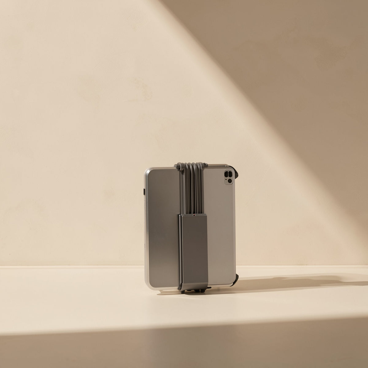 Rotaperch Rotary Phone and Tablet Stand folded flat, gray, holding a tablet from behind on a sunlit ledge