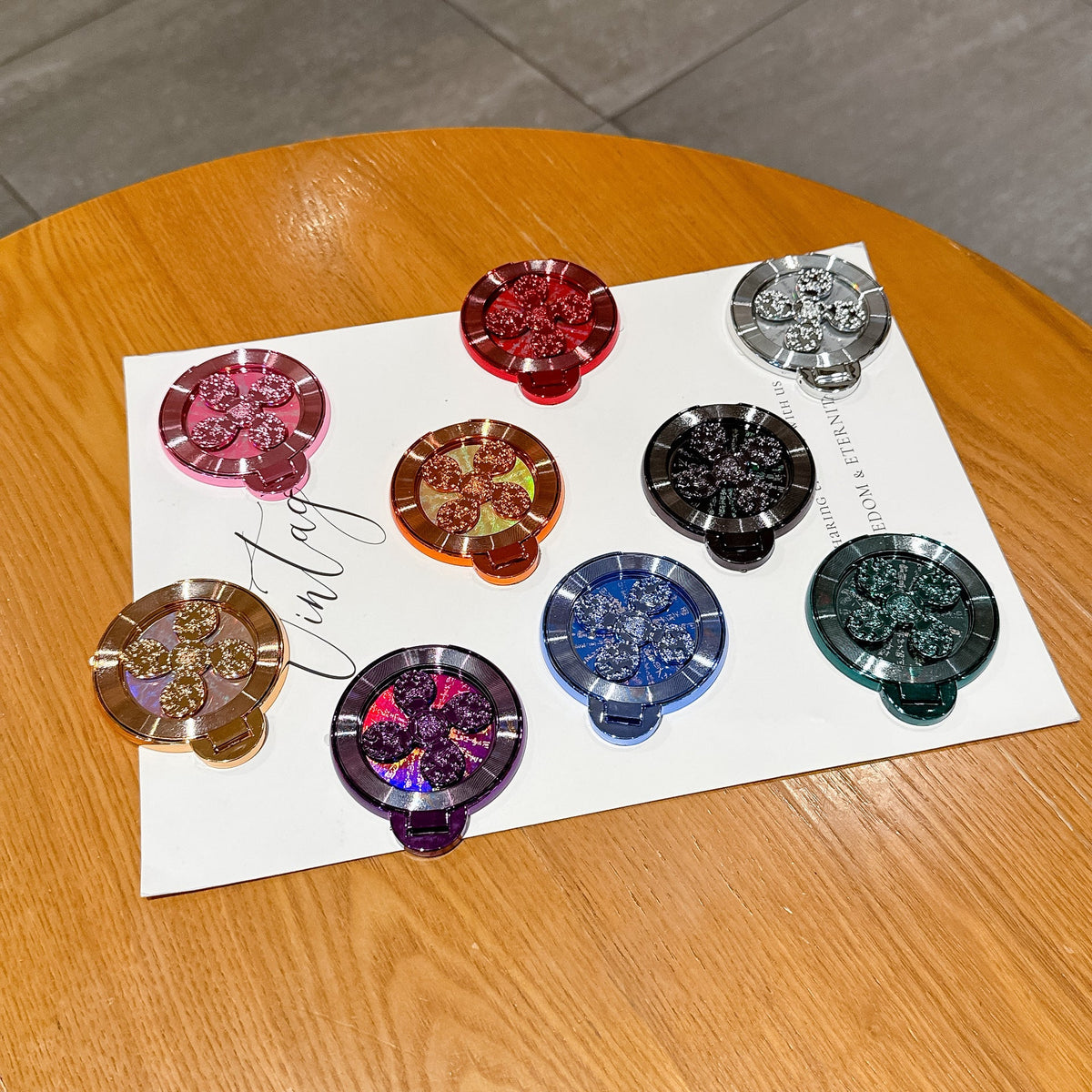 Discperch Desktop Phone Stand in nine colours with glittery flower centres laid out on a white sheet on a table