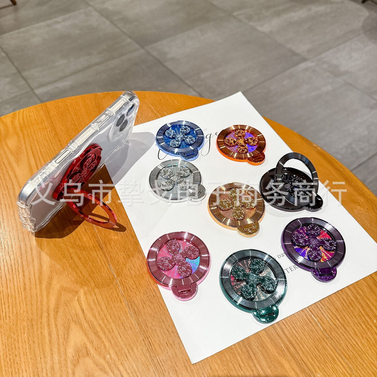 Discperch – Phone propped sideways on the red stand's folded ring, with eight other colours on the table beside it