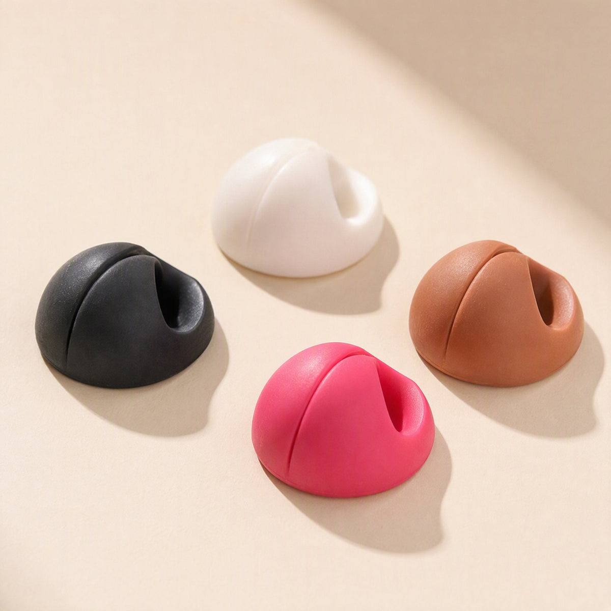 Cordslot Plastic Single-Hole Cable Organizer in black, white, brown and pink on a beige surface