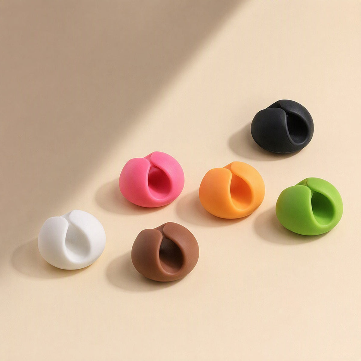 Cordslot – Six round self-adhesive cable clips in white, pink, brown, black, orange and green on a cream background