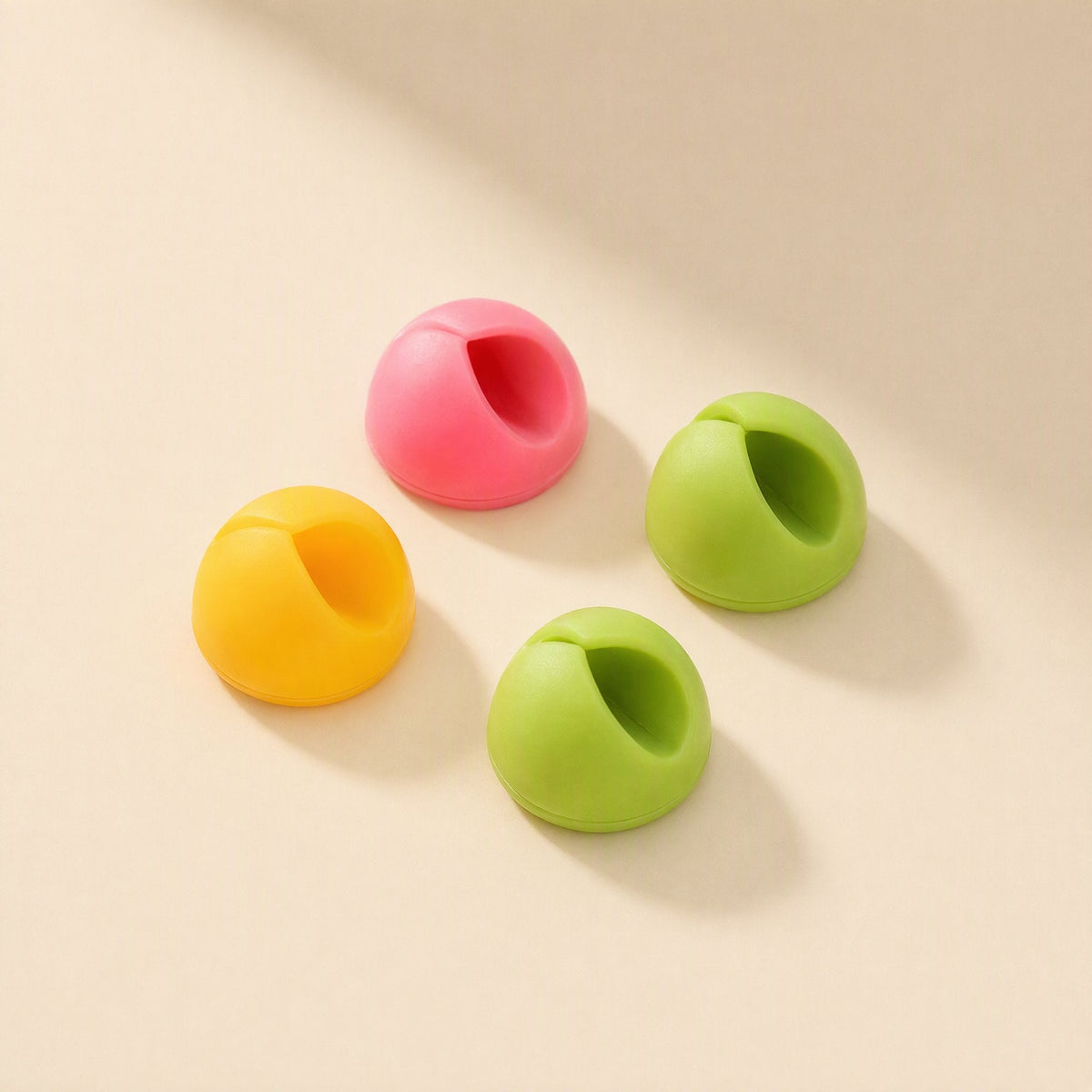 Cordslot – Four dome-shaped cable holders in yellow, pink and two shades of green, angled to show the cable slot