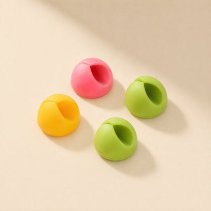 Cordslot – Four dome-shaped cable holders in yellow, pink and two shades of green, angled to show the cable slot