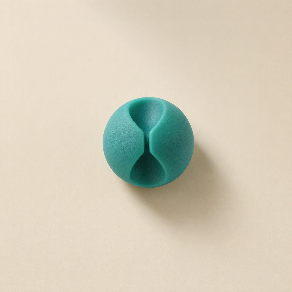 Cordslot – Single teal cable organizer from above, showing its hourglass-shaped slot on a beige background