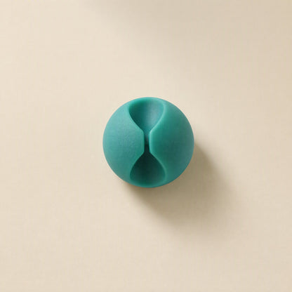 Cordslot – Single teal cable organizer from above, showing its hourglass-shaped slot on a beige background