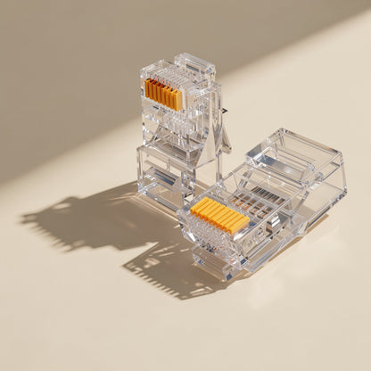 Jackmate RJ45 network cable connectors, two clear plugs with gold contacts casting shadows on a cream surface