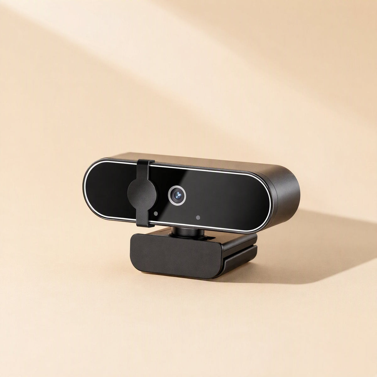 Pixelsharp – Low side angle of the black webcam on its clip base, casting a soft shadow on a peach backdrop