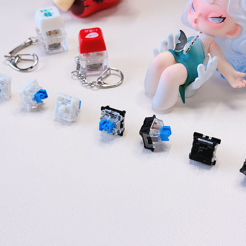 Crispop – Close-up of keychain switches and loose blue switches in a row, with a doll seated in the background