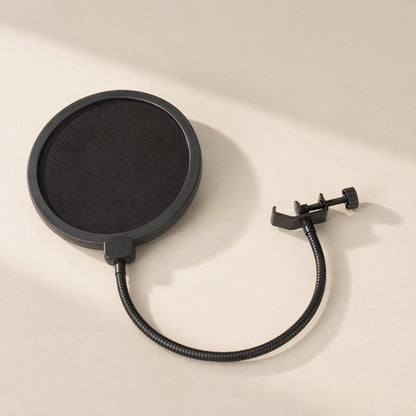 Streamveil – Black round pop filter with gooseneck and C-clamp lying on a beige surface in soft diagonal light