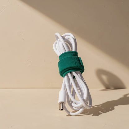 Green Colortie cable tie wrapped around a coiled white charging cable with a barrel connector