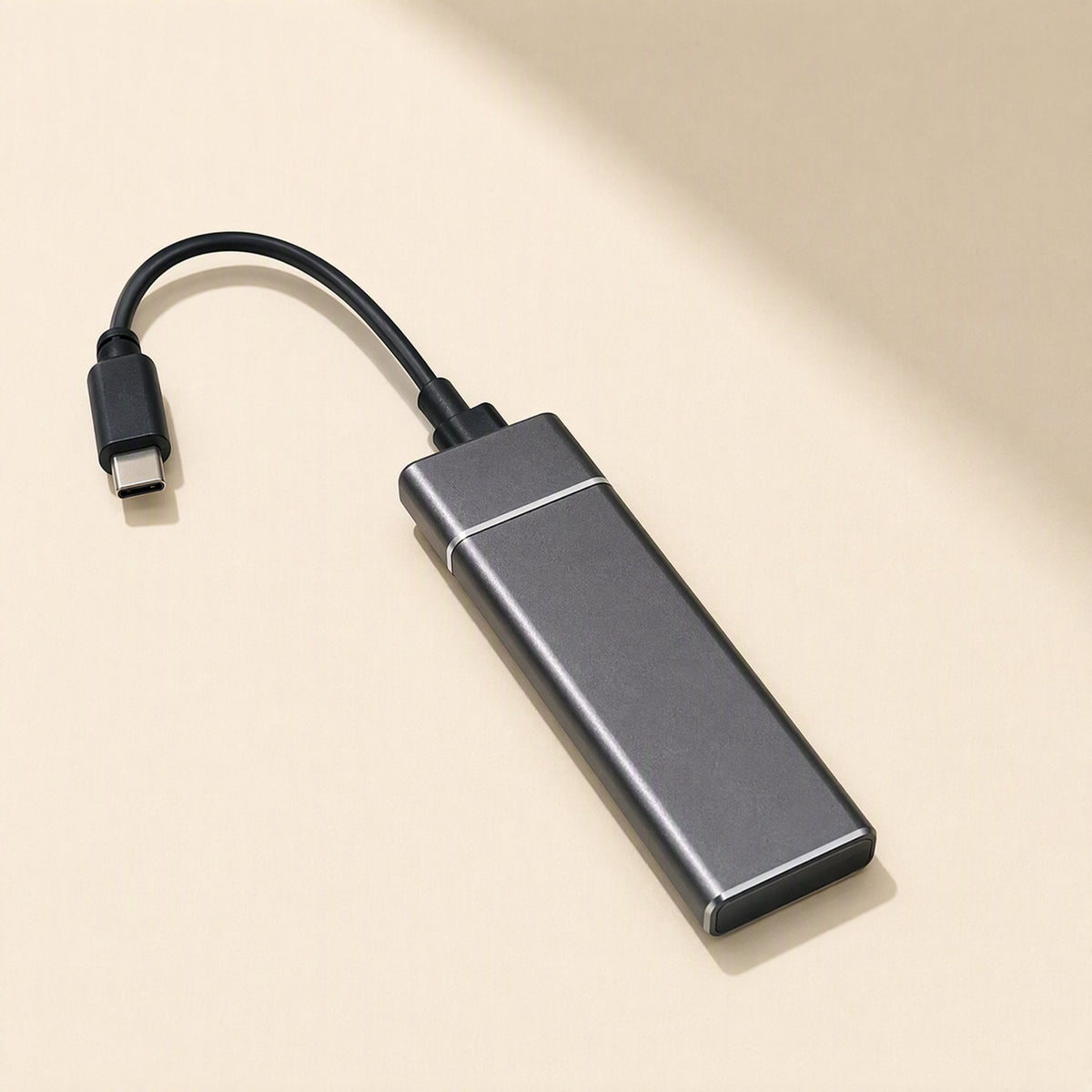 Drivevault – Grey portable solid state drive with a short attached USB-C cable lying on a cream background