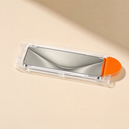 Clearshield – Side view of the glass protector seated in its clear installation tray with orange pull tab on a cream surface