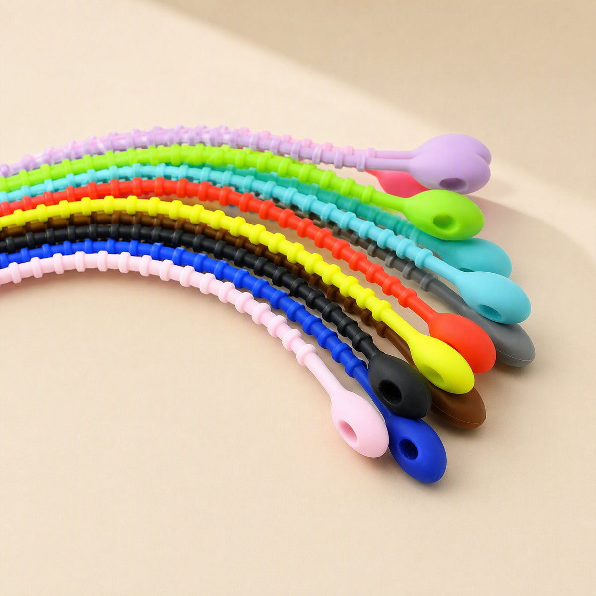 Cordtame – Row of silicone cable ties in rainbow colours curving across a beige surface, ends with oval fastener heads