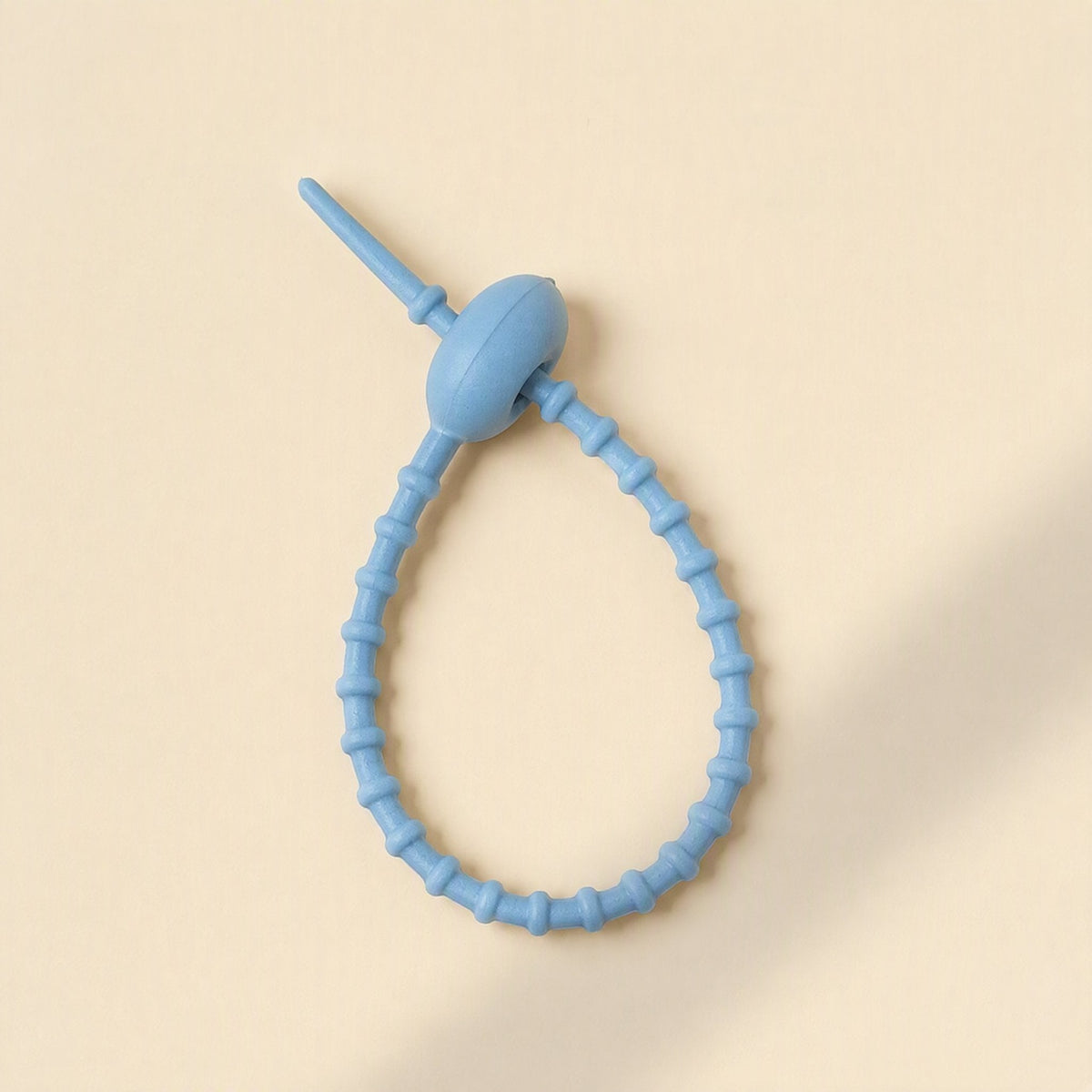 Cordtame Cable Organizer – single light blue silicone tie looped into a teardrop shape on a cream background