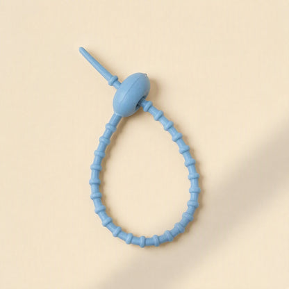 Cordtame Cable Organizer – single light blue silicone tie looped into a teardrop shape on a cream background