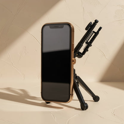 Alufold – Black folding tripod-style stand propping a gold-edged smartphone upright against a textured beige wall