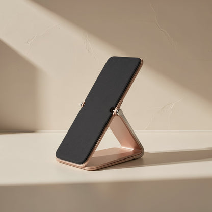 Alufold – Rose-gold folding stand with a black padded rest, set at a reclined angle in soft side light