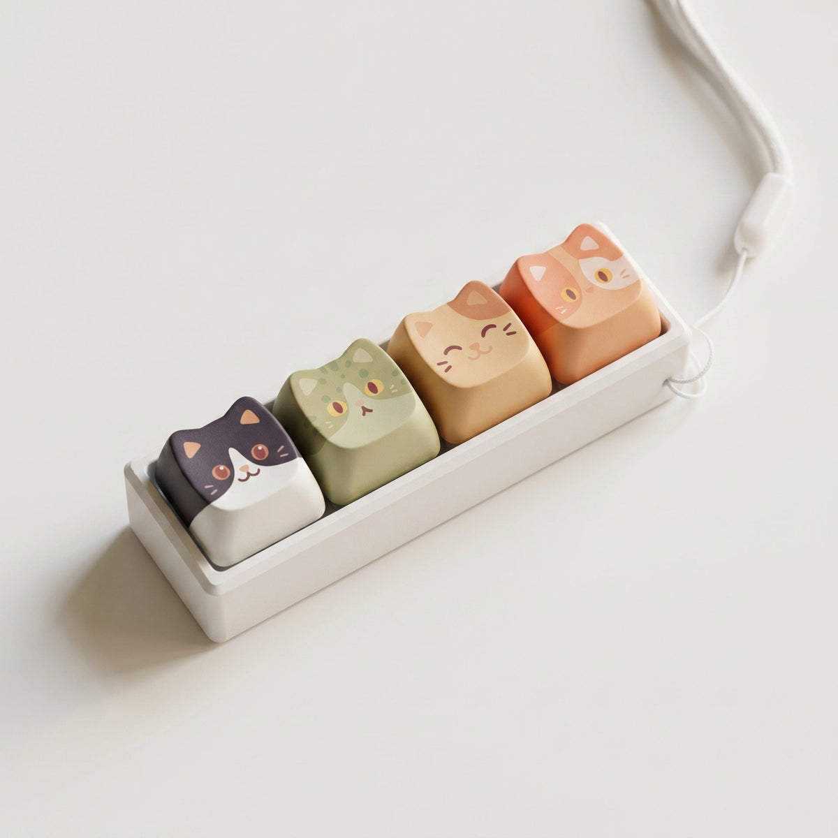 Furrkey – Row of four cat keycaps in a white holder with a looped white cord, seen from above on a plain white surface