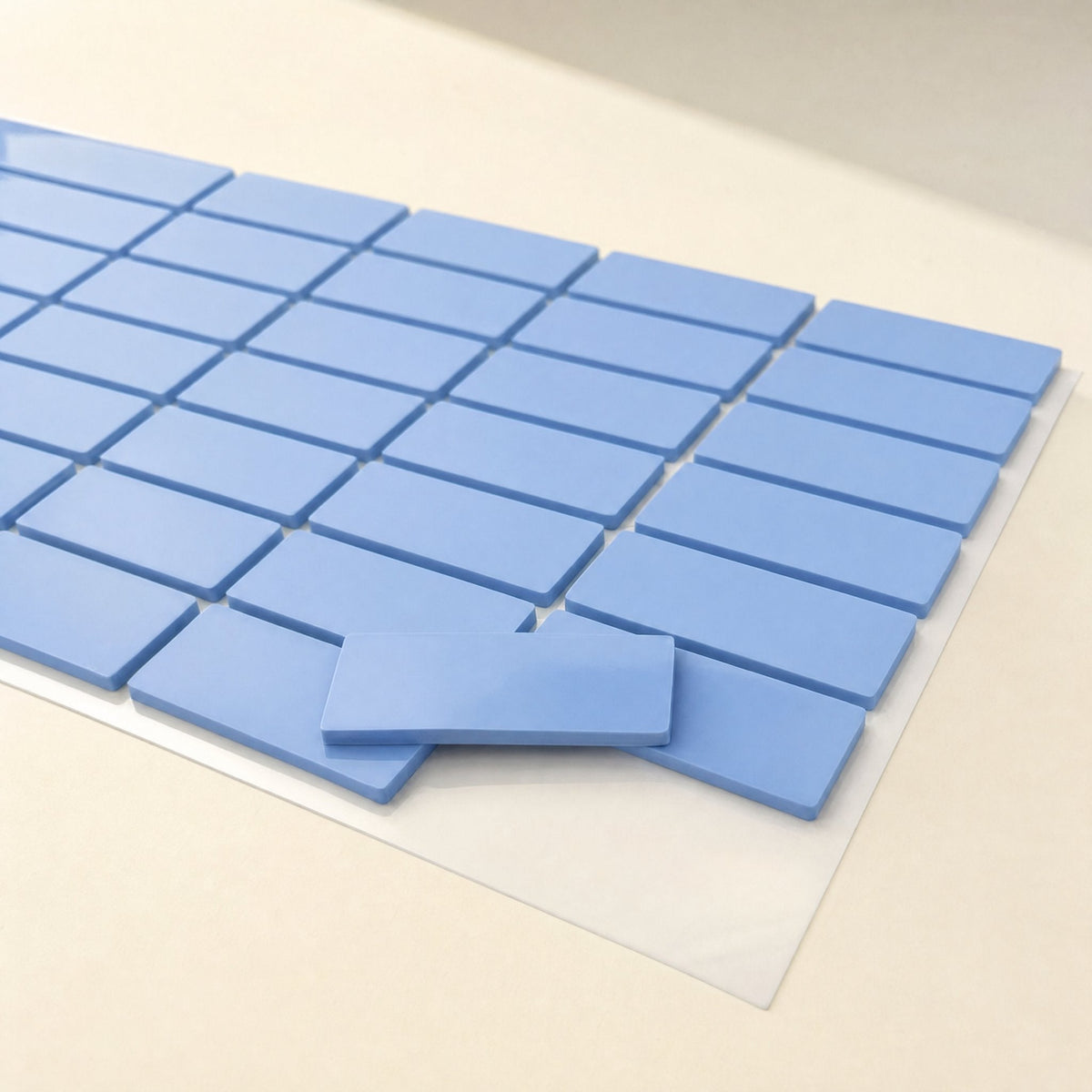 Thermaseal Silicone Thermal Pad cut into rows of blue rectangles on a clear backing sheet, one piece lifted