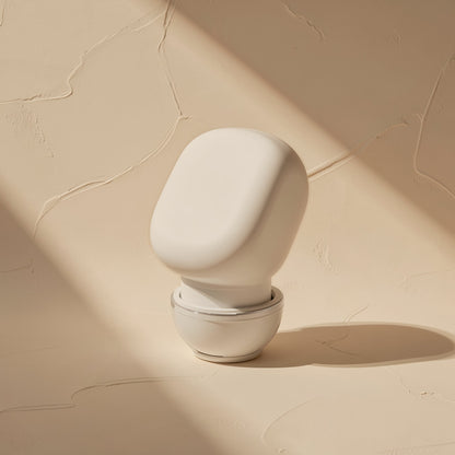 Solehear – White single earbud on its side with a rounded matte shell and clear ear tip, against textured beige plaster