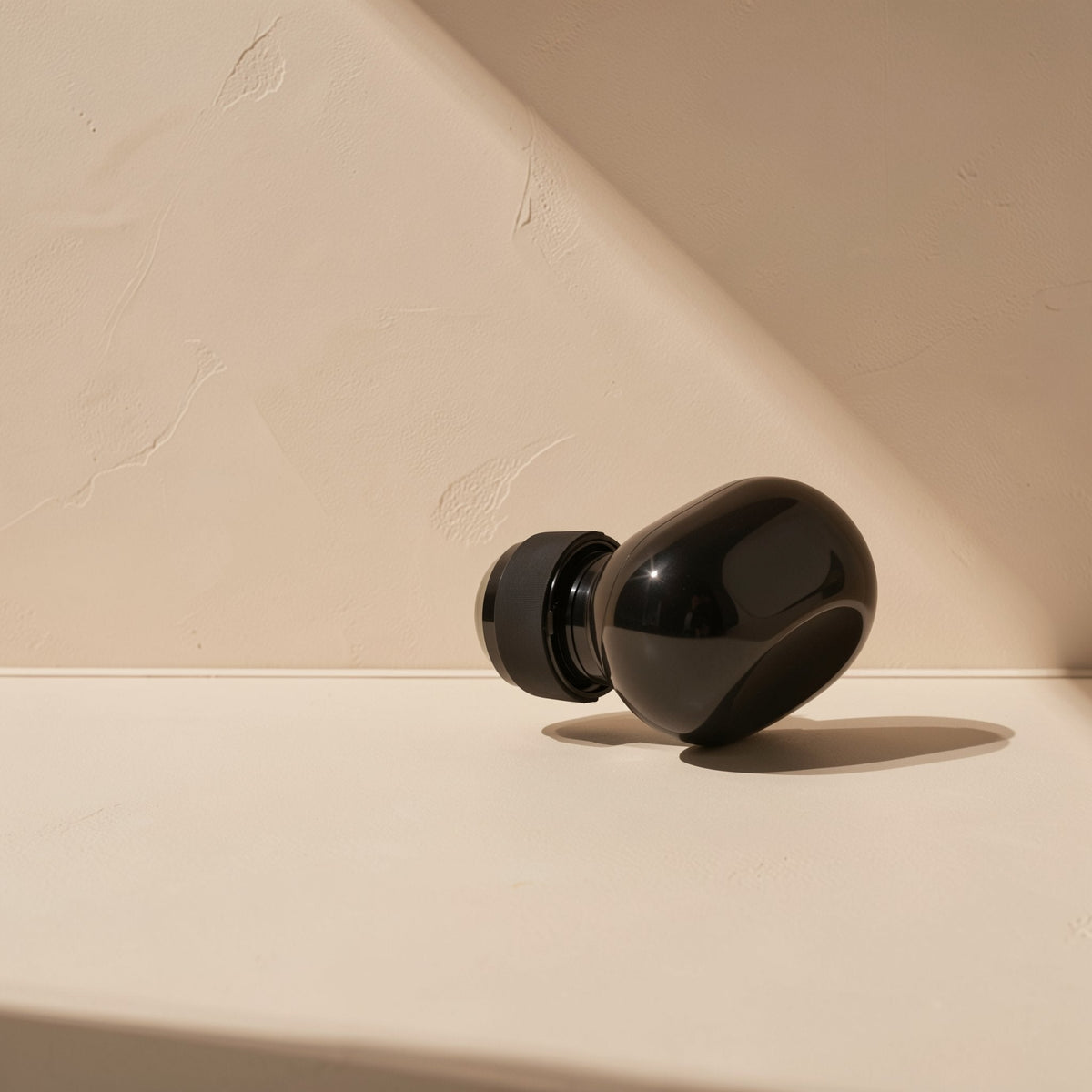 Solehear – Glossy black earbud lying on its side with a black silicone ear tip, in warm sunlight on a beige surface