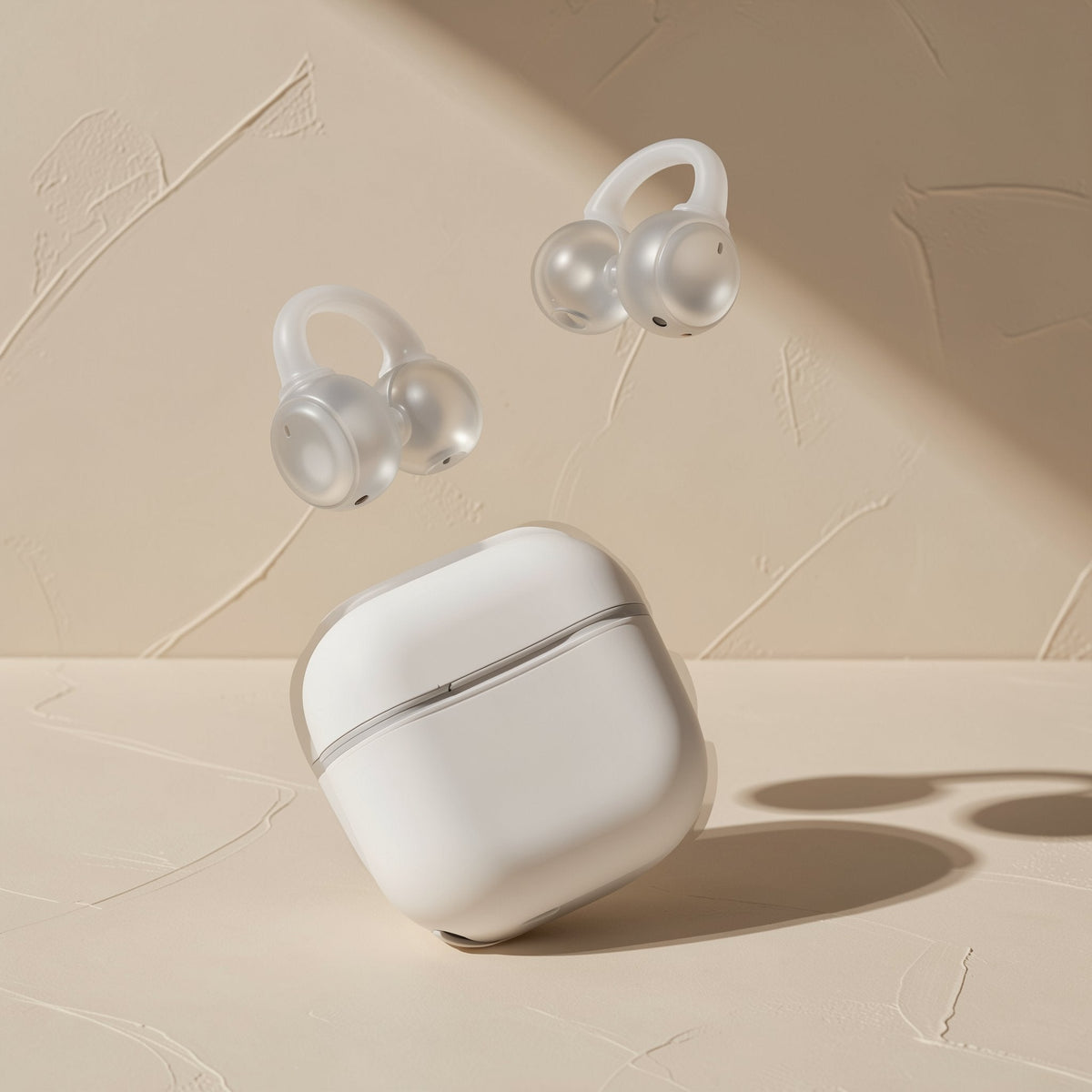 Clipbeat – Pair of translucent white clip-on earbuds hovering above a closed white charging case on a beige surface