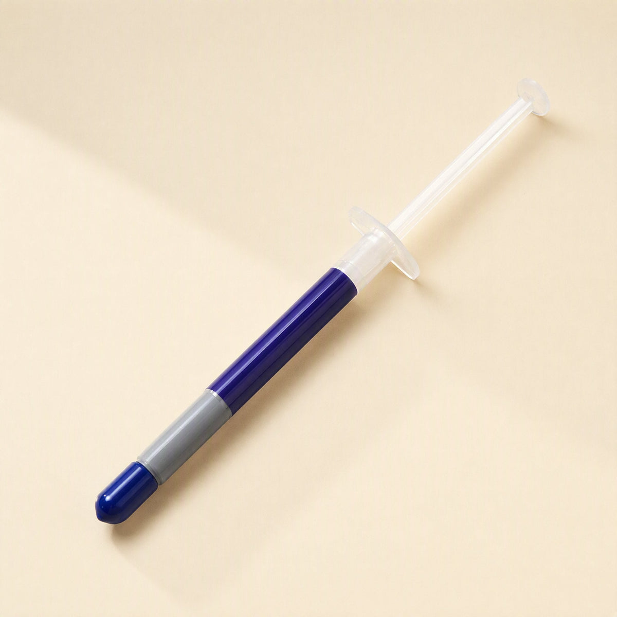 Heatbond – Single syringe with blue cap and gray band lying diagonally on a beige background