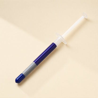 Heatbond – Single syringe with blue cap and gray band lying diagonally on a beige background
