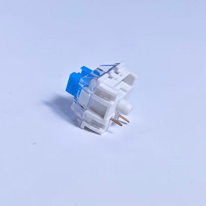 Clickzen – Single white switch with clear top housing and blue stem, angled view showing two gold pins