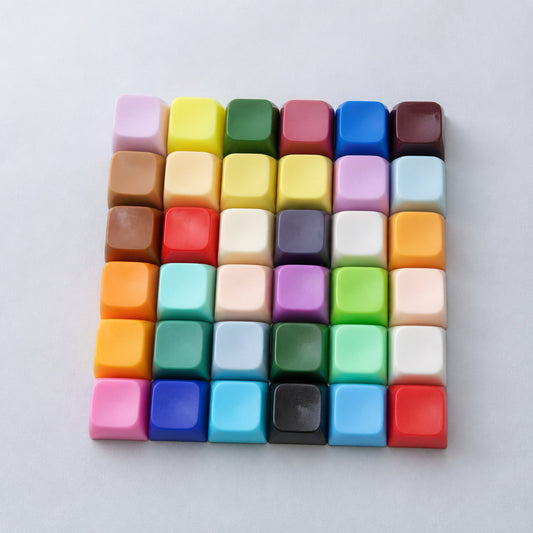 Top-down view of 36 Capscript keycaps in a rainbow of colours, laid out in a six-by-six square on grey