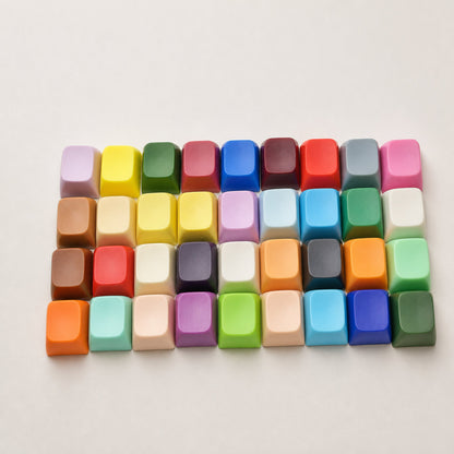 Capscript – Four rows of colourful blank keycaps in pink, yellow, green, red, blue and brown on a white surface