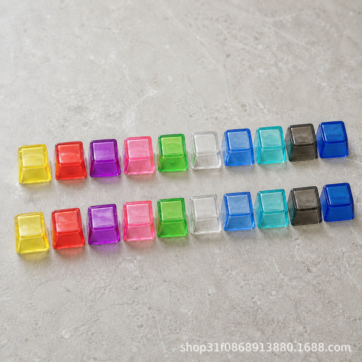 Clarion – Two rows of ten translucent blank keycaps in assorted colours lined up side by side on a gray textured surface