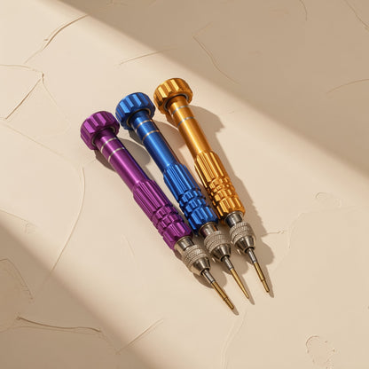 Screwwise – Three screwdrivers in purple, blue and gold lying side by side on a beige surface in angled sunlight