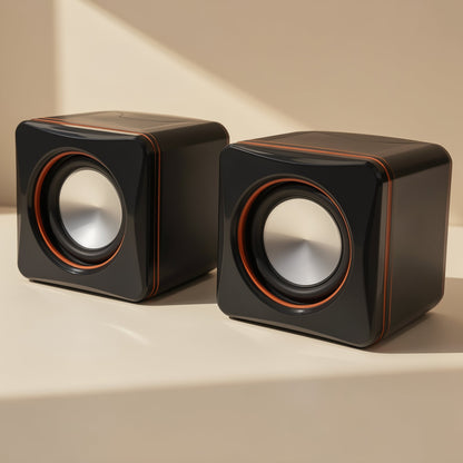 Desktune Mini Computer Speakers, a pair of glossy black cube speakers with orange trim, angled on a cream surface