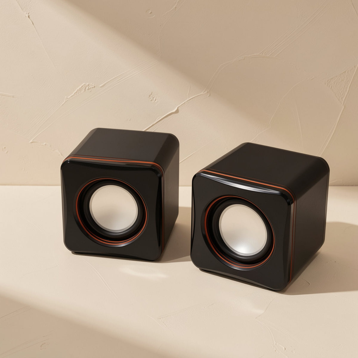 Desktune – Two black cube speakers with silver-white cones and thin orange rings, set against a textured beige wall