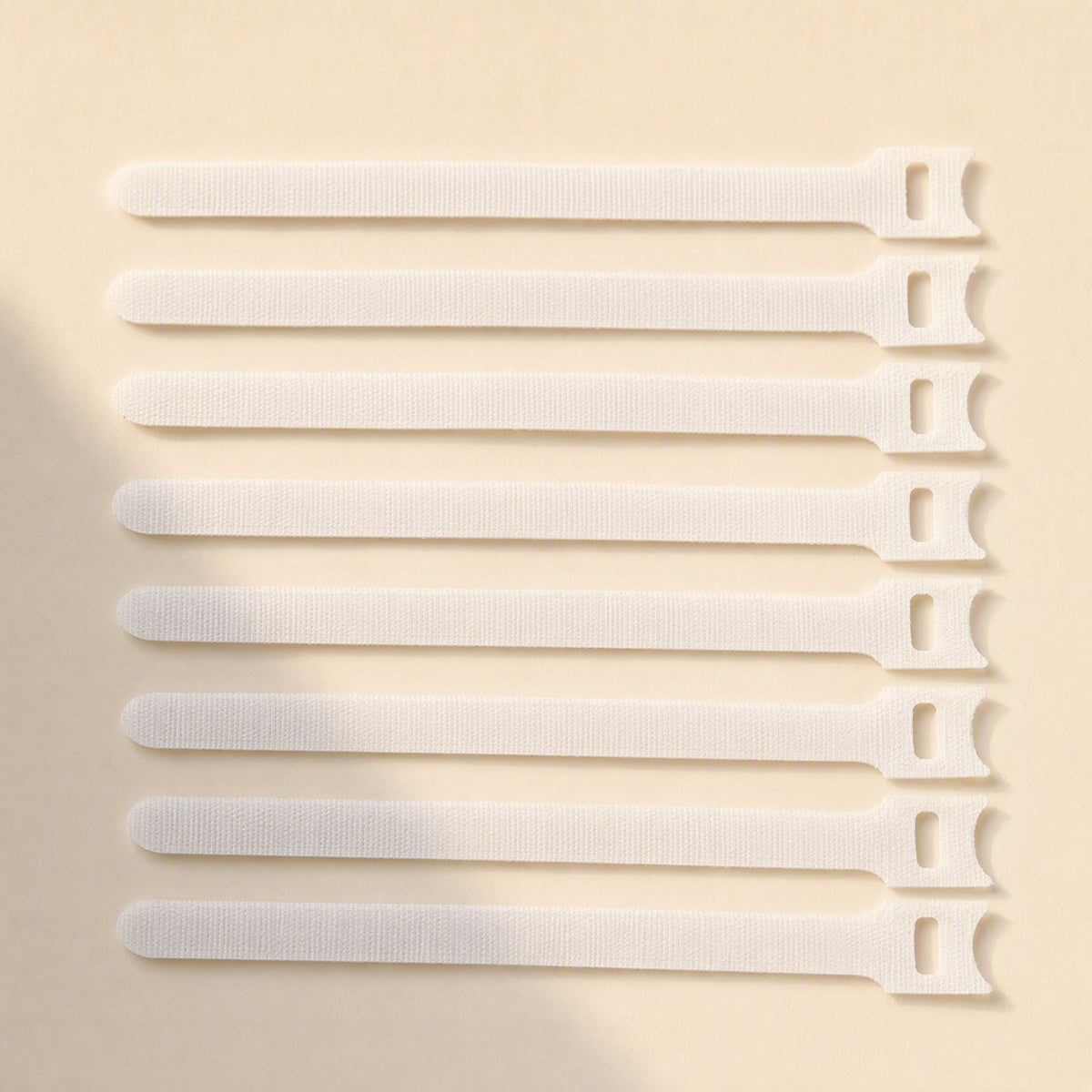 Loopmate – Eight white hook-and-loop cable ties lined up in a neat row on a cream background