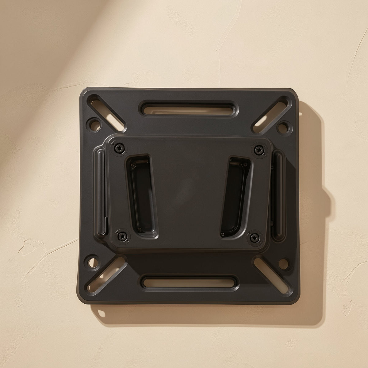 Wallpivot Iron Monitor Wall Mount in black, top-down view with slotted holes on a cream wall