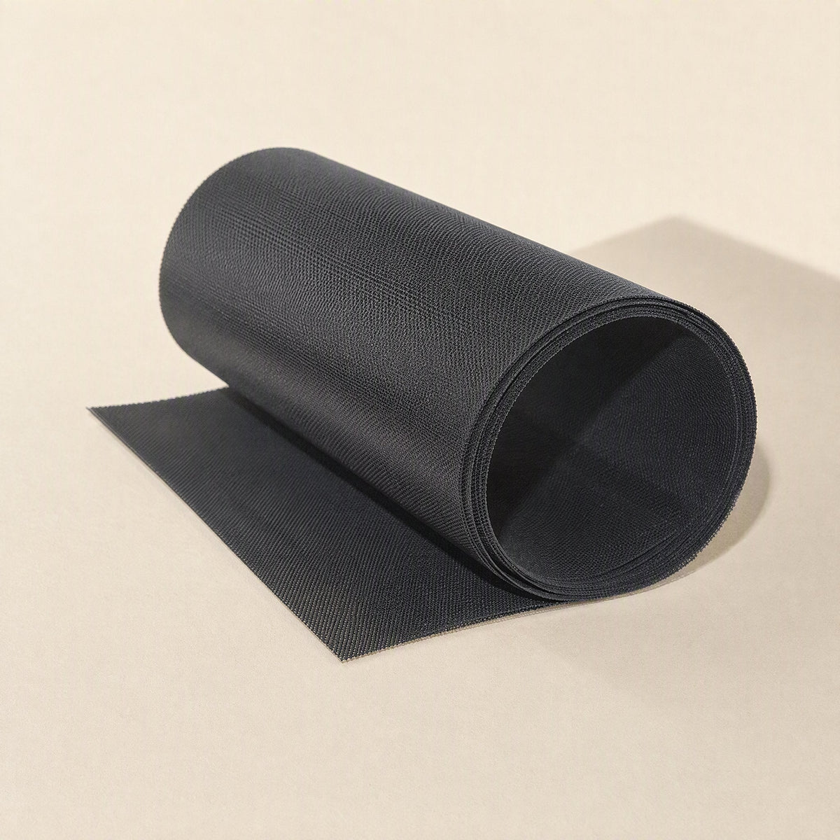Fanfilter – Black mesh roll with a loosely unrolled end, viewed from a slightly different angle on a beige surface